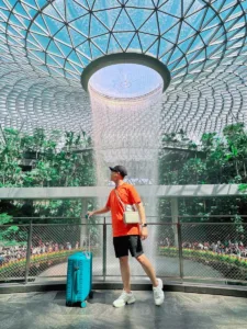 A man with luggage stands by the iconic Jewel Changi Airport waterfall in Singapore.